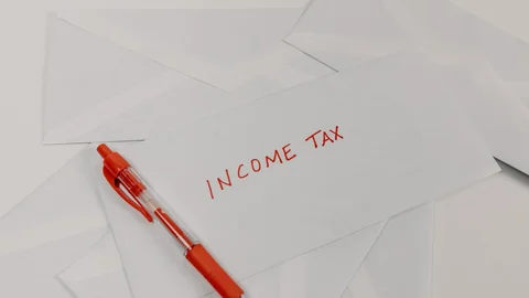 Sobre blanco con las palabras «Income Tax» escritas en rojo, junto a un bolígrafo rojo y otros sobres.