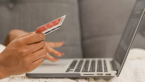 Una persona sostiene una tarjeta bancaria frente a un portátil durante una compra online.