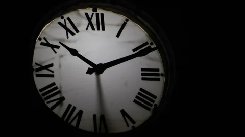 Reloj analógico iluminado sobre un fondo negro.