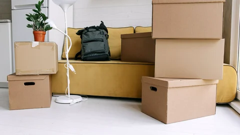 Varias cajas de cartón apiladas y una mochila en un salón preparado para una mudanza.